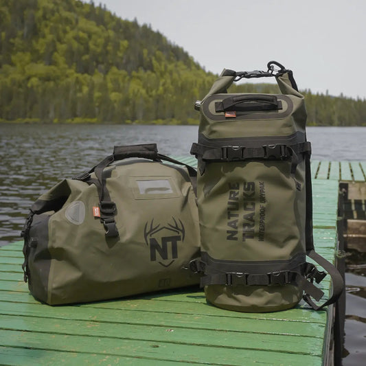 Two green outdoor bags with 'Nature Tracks' branding on a wooden dock by a lake.